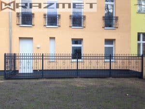 Schmiedeeiserner Zaun vor gelbem Wohngebäude.